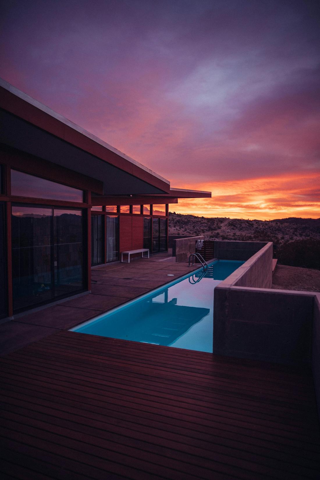 A lit pool and stone deck at dusk, mountains behind