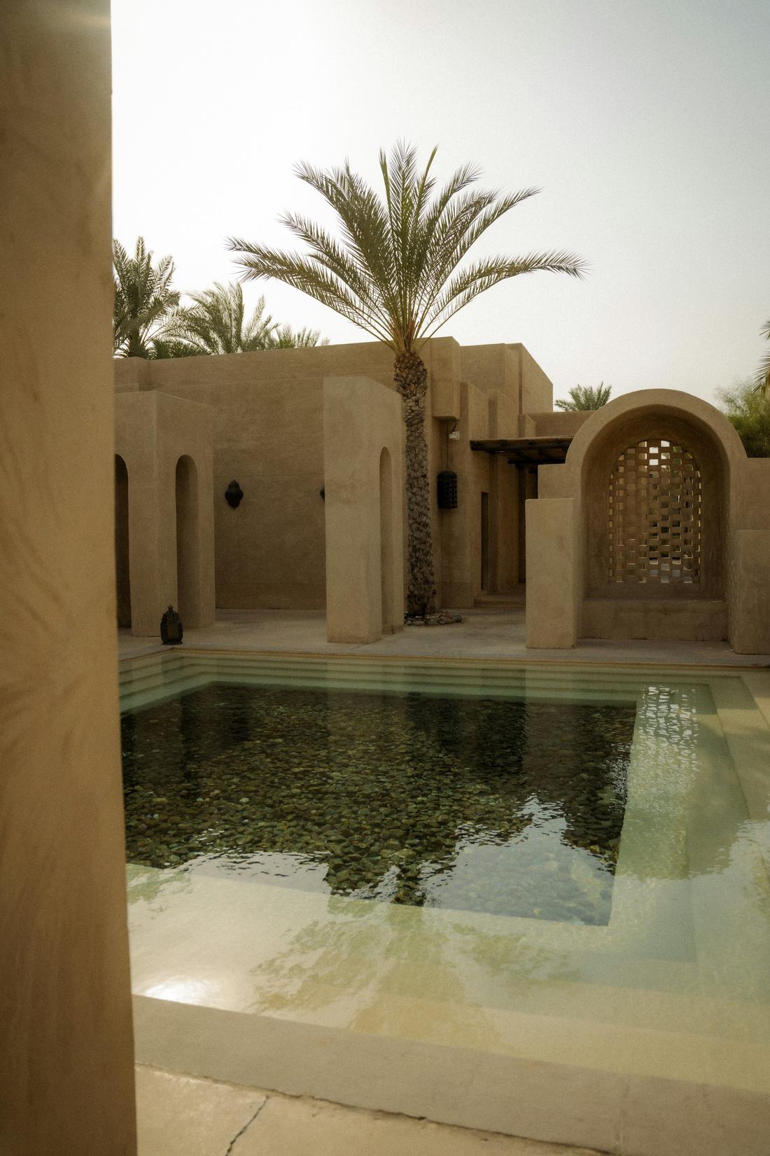 A small courtyard pool between adobe walls and a palm