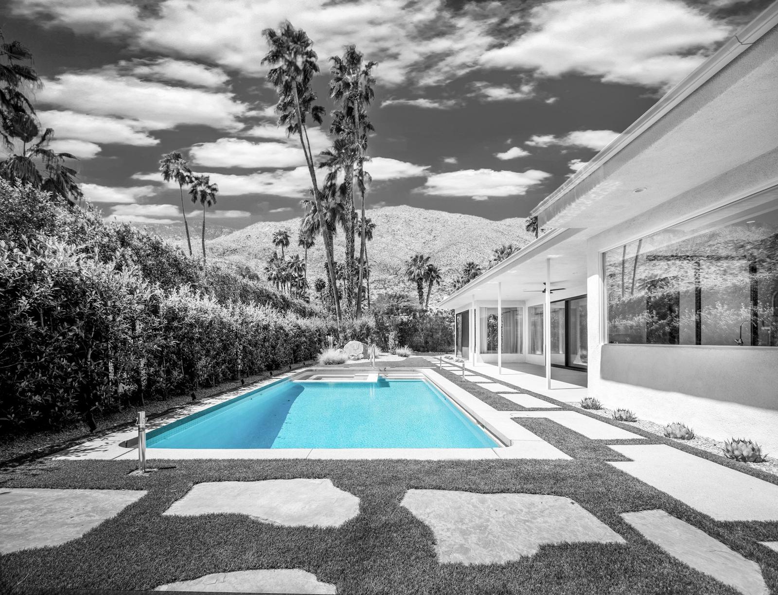 Blue geometric pool beside a modern house, palms and mountains